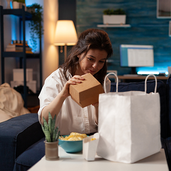 Woman on sofa unpacking burger box from paper takeaway bag