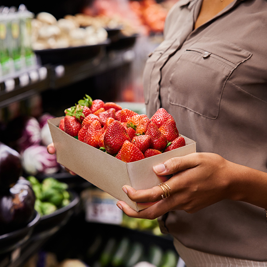 Frau steht in einem Supermarkt und hält eine Schachtel Erdbeeren in der Hand