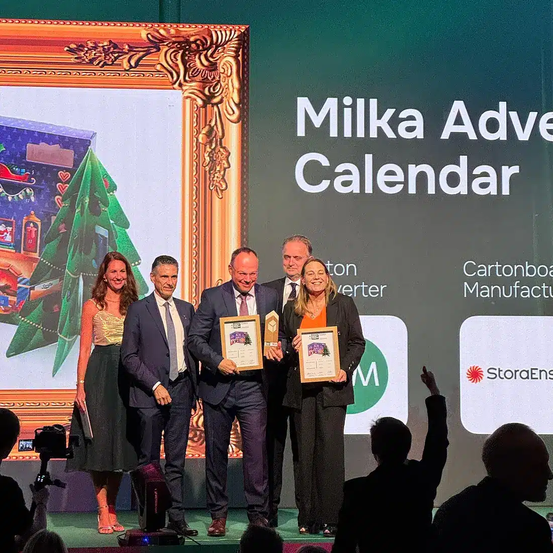 MM team winners standing on stage holding certificates at the European Carton Excellence Awards 2025, with a presentation screen in the background displaying “Milka Advent Calendar.”